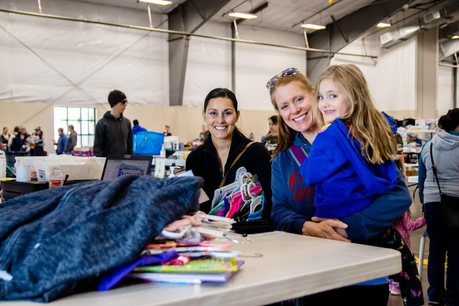 A mom and her daughter stand at the check out counter with another mom at the local JBF sale.