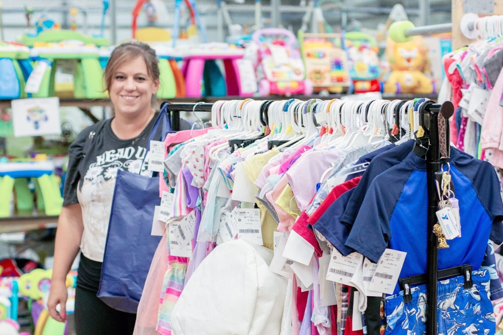 a woman consiging stands be her rolling rack of clothing to sell